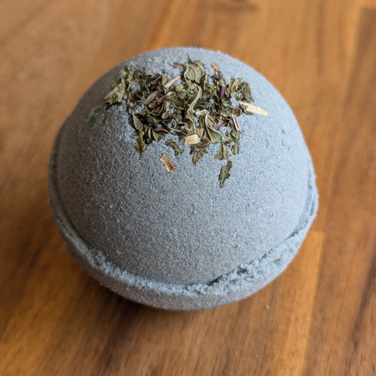 light blue aromatherapy bath bomb with mint herbs on a wooden surface